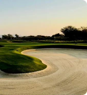 Un trou de golf qui contourne un large bunker de sable dans la lumière du soir.